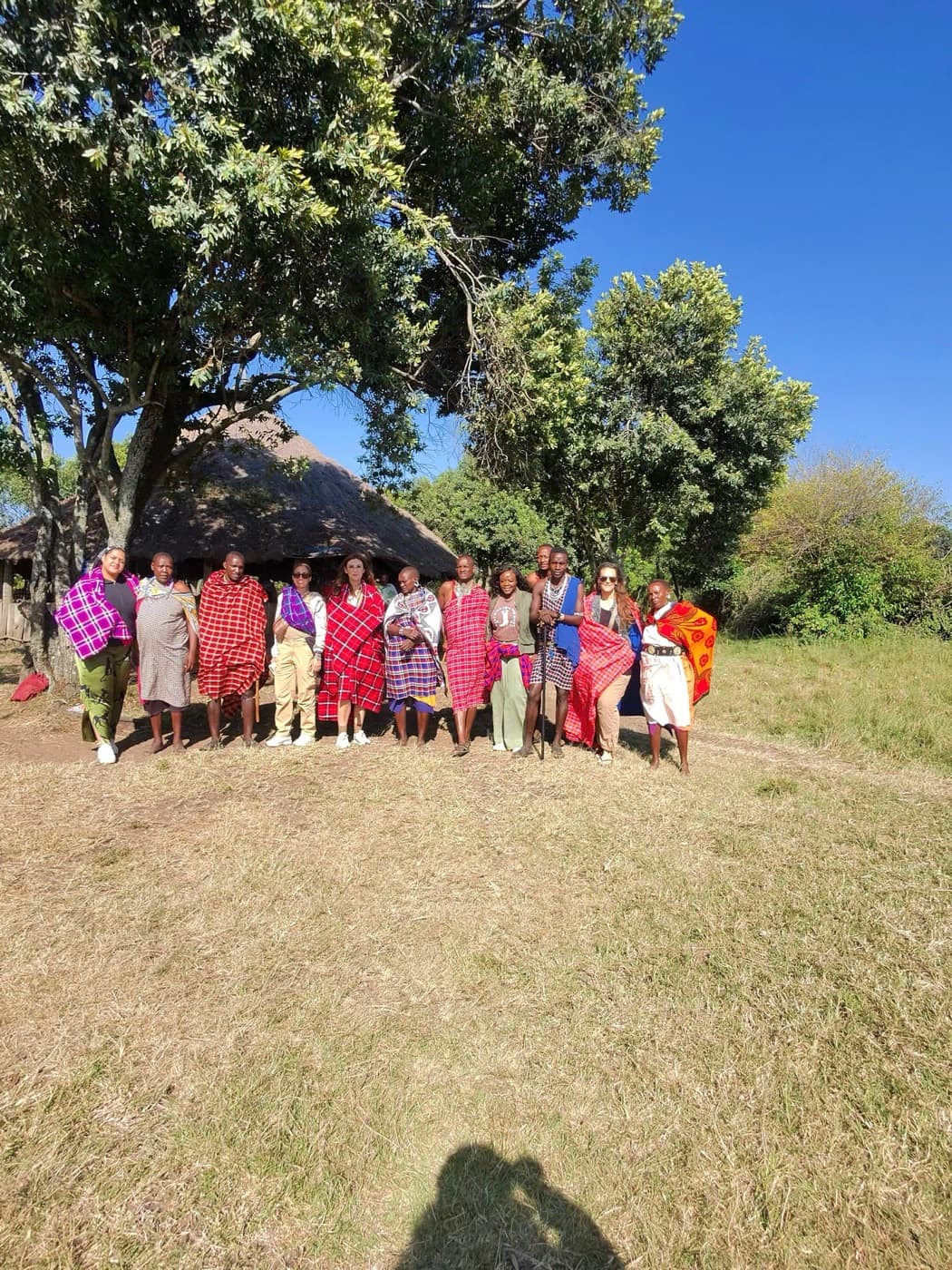 Travelers and Maasai hosts gathered outdoors in colorful shukas